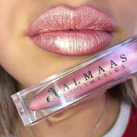 תקריב של שפתי אישה המורחת שפתון מטאלי עמיד בגוון 61. היא מחזיקה ליד פיה שפופרת שקופה שעליה הכיתוב "ALMAAS COSMETICS", והגוון הוורוד המנצנץ על שפתיה תואם לצבע שבשפופרת. | אלמאס קוסמטיקה – מתנה מושלמת של טיפוח ויוקרה