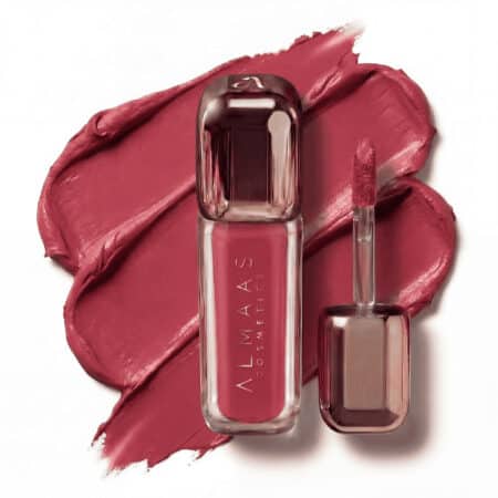 שפופרת של שפתון נוזלי מבית ALMAAS Cosmetics והמברשת המצורפת אליה מונחות על דוגמית קרמית של שפתון עשיר בגוון ורוד-סגול, ויוצרות רקע בולט ומרקמי. שפופרת השפתון שקופה, חושפת את צבע השפתון שבתוכה, ומעוצבת באלגנטיות. | אלמאס קוסמטיקה – מתנה מושלמת של טיפוח ויוקרה