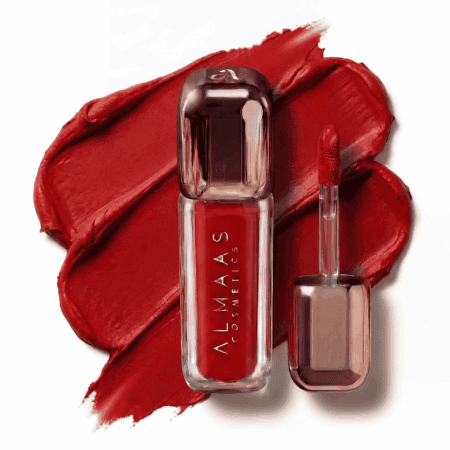שפופרת מבריקה של שפתון נוזלי אדום מבית ALMAAS Cosmetics, עם מכסה כסוף, מונחת על כתם של שפתון אדום עז. מברשת המריחה, המצופה באדום, מונחת לצד השפופרת. הרקע הלבן מדגיש את הצבע העז. | אלמאס קוסמטיקה – מתנה מושלמת של טיפוח ויוקרה