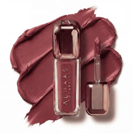 שפופרת בצבע זהב ורוד של שפתון נוזלי מבית ALMAAS Cosmetics מונחת על כתם של שפתון סגול-ורוד. השפופרת מעוצבת בקווים חלקים, עם קצוות מלוטשים ודפנות שקופות המציגות את צבע השפתון. מברשת המריחה התואמת מונחת לצדה, כשעל קצה המברשת ניכר צבע השפתון. | אלמאס קוסמטיקה – מתנה מושלמת של טיפוח ויוקרה