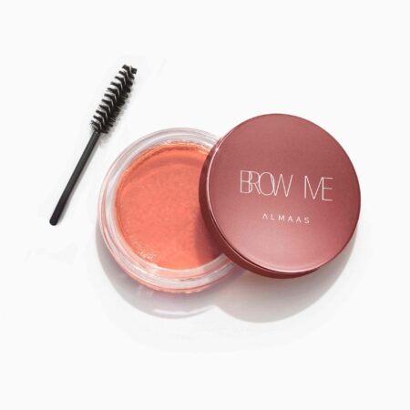 ערכת טיפוח לגבות הכוללת מיכל עגול בצבע אדום-ורוד שעליו הכיתוב "BROW ME ALMAAS" לצד מברשת גבות. המיכל פתוח, וחושף בתוכו מוצר לגבות בצבע אפרסק. הפריטים מוצגים על רקע לבן. | אלמאס קוסמטיקה – מתנה מושלמת של טיפוח ויוקרה