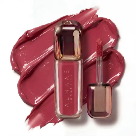 שפופרת של שפתון נוזלי מבית ALMAAS Cosmetics והמברשת המצורפת אליו מונחות על גבי דוגמיות שפתון בצבע סגול-ורוד. האריזה מתכתית בגווני זהב ורוד, וגווני השפתון תואמים לדוגמיות שמתחתיה. | אלמאס קוסמטיקה – מתנה מושלמת של טיפוח ויוקרה