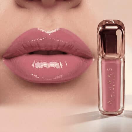 תקריב של שפתיים ורודות בהירות ומבריקות עם עור חלק. לצד השפתיים מונח שפופרת של גלוס לשפתיים מבית ALMAAS COSMETICS בגוון ורוד תואם, עם מיכל שקוף ומכסה בצבע חום-אפור על רקע בז'. | אלמאס קוסמטיקה – מתנה מושלמת של טיפוח ויוקרה
