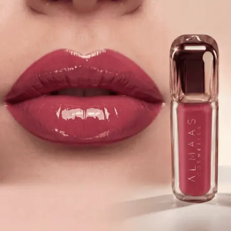 תקריב של שפתיים מלאות ומבריקות, המרוחות בשפתון אדום-ורוד. לצד השפתיים מוצג שפופרת תואמת של שפתון נוזלי מבית ALMAAS Cosmetics, באריזה אלגנטית ושקופה עם מכסה מתכתי. הרקע ניטרלי ומטושטש. | אלמאס קוסמטיקה – מתנה מושלמת של טיפוח ויוקרה