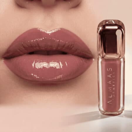 תקריב של שפתיים מלאות ומבריקות, המרוחות בשפתון ורוד ניוד. לצד השפתיים מונח שפופרת תואמת של שפתון מבית ALMAAS Cosmetics, עם מכסה שקוף ואריזה אלגנטית, המוצגת בעמידה על משטח בהיר ומבריק. | אלמאס קוסמטיקה – מתנה מושלמת של טיפוח ויוקרה