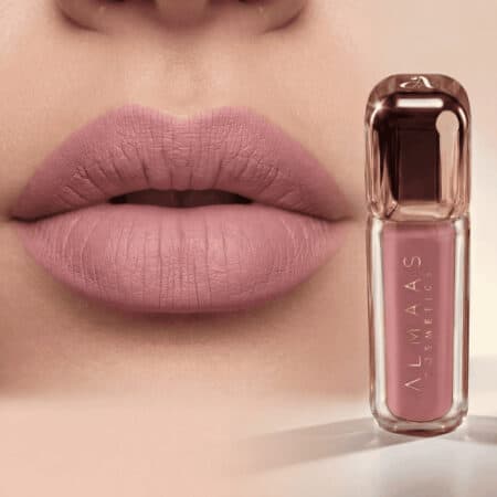 תקריב של שפתיים מלאות המרוחות בשפתון ורוד-סגול מט. לצד השפתיים מונח שפופרת שקופה של שפתון נוזלי מבית AlMaaS Cosmetics בגוון תואם, עם מכסה מודרני בצבע זהב-ורוד ולוגו אלגנטי. הרקע רך וניטרלי. | אלמאס קוסמטיקה – מתנה מושלמת של טיפוח ויוקרה