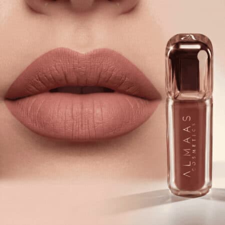 תקריב של שפתיים המרוחות בשפתון ניוד מט, בעל מרקם חלק וקווי מתאר חדים. לצד השפתיים מונחת שפופרת שפתון שעליה הכיתוב "ALMAAS COSMETICS" באותיות זהב ורוד, בתוך אריזה שקופה. הרקע בצבע בז' רך, המשתלב היטב עם צבע השפתיים. | אלמאס קוסמטיקה – מתנה מושלמת של טיפוח ויוקרה