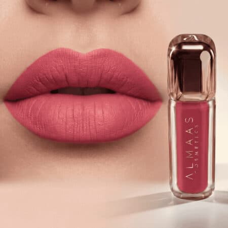 תקריב של שפתי אישה המורחות בשפתון מט בגוון ורוד. לצד השפתיים מונח שפופרת תואמת של שפתון מבית ALMAAS Cosmetics, בעלת מארז שקוף ולוגו אלגנטי. הרקע ניטרלי, וממקד את תשומת הלב במוצר ובשפתיים. | אלמאס קוסמטיקה – מתנה מושלמת של טיפוח ויוקרה