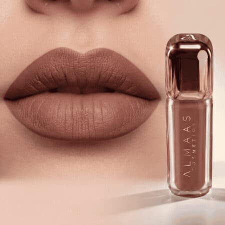 תקריב של שפתיים מלאות המרוחות בשפתון חום-ניוד מט. בצד ימין, על רקע בז' רך, נראית שפופרת שפתון חום-ניוד תואמת עם הכיתוב "ALMAAS COSMETICS" ומכסה שקוף. | אלמאס קוסמטיקה – מתנה מושלמת של טיפוח ויוקרה