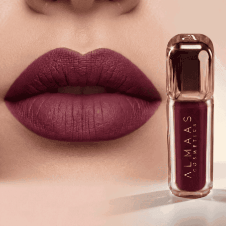 תקריב של שפתי אישה המרוחות בשפתון בורדו עמוק במראה מט. לצד השפתיים מונחת שפופרת שפתון תואמת, שעליה הכיתוב "ALMAAS COSMETICS" באותיות לבנות, עם אריזה אלגנטית ומודרנית ומכסה שקוף. הרקע ניטרלי ומטושטש קלות. | אלמאס קוסמטיקה – מתנה מושלמת של טיפוח ויוקרה