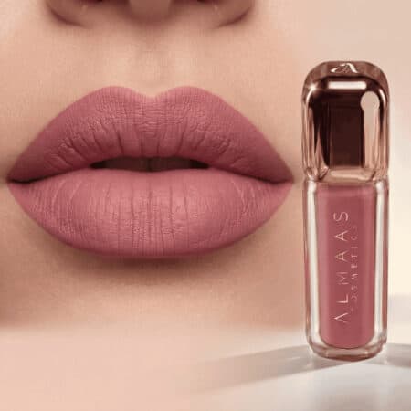 תקריב של שפתי אישה המרוחות בשפתון סגול-ורוד מט, כשהן פתוחות קלות. לצד השפתיים מונחת שפופרת שפתון תואמת עם הכיתוב "ALMAAS COSMETICS", בעלת גוף שקוף ומכסה מתכתי, המציגה את הגוון הוורוד הבהיר שבתוכה. | אלמאס קוסמטיקה – מתנה מושלמת של טיפוח ויוקרה